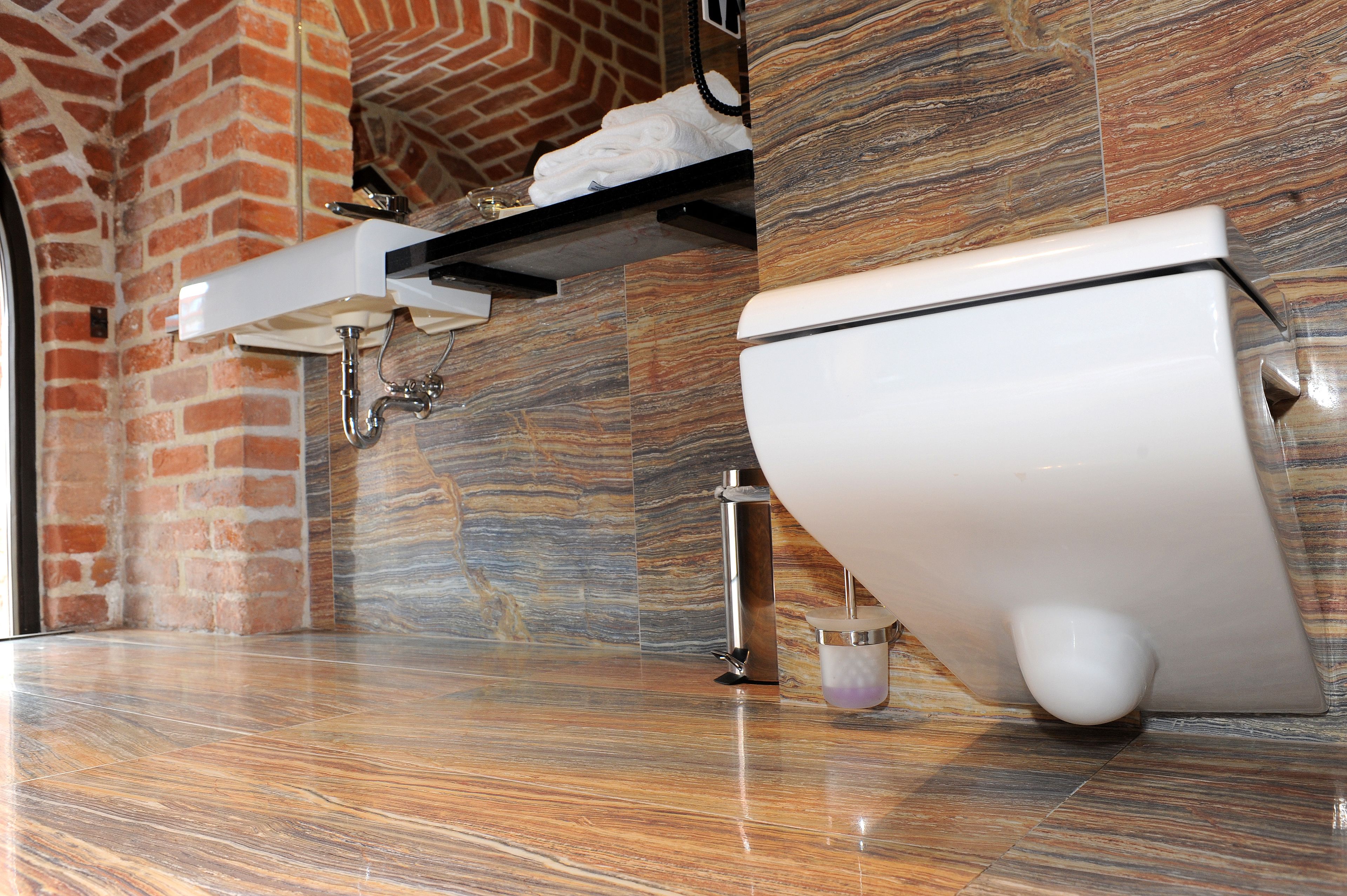 Une salle de bain au design moderne, avec un sol en marbre, des toilettes blanches et un mur en briques.