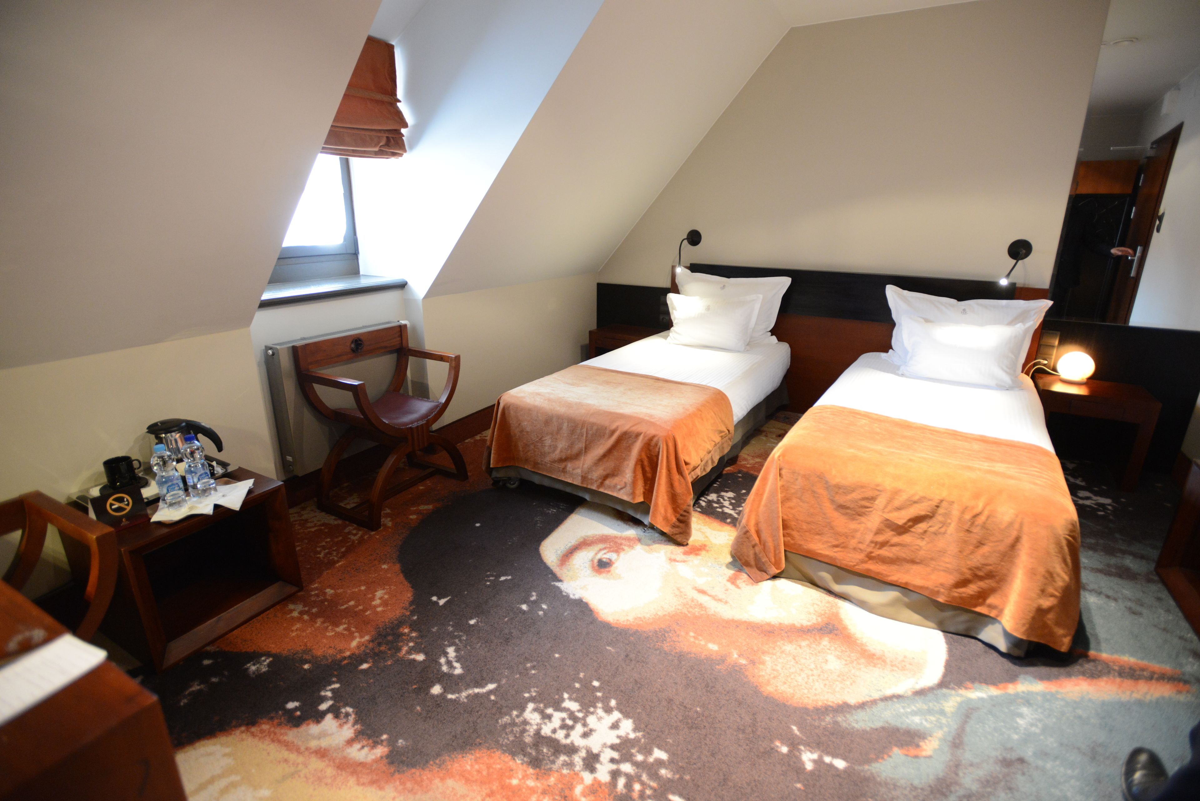 A hotel room with two beds, a desk, a chair, and a large window.