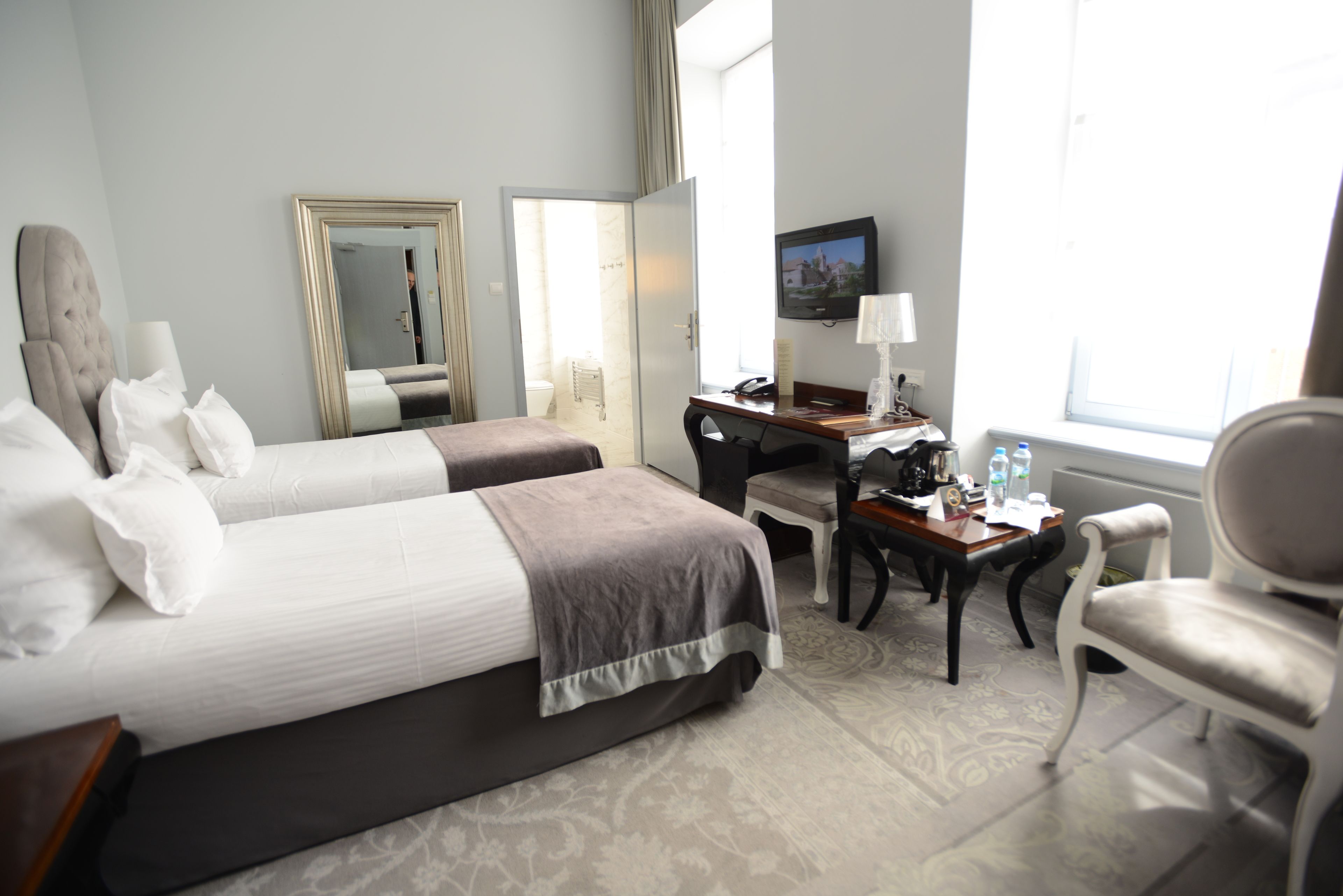 A hotel room with two beds, a desk, a chair, a TV, and a window.