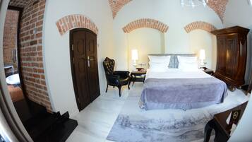 A room with a brick ceiling, a bed with a white headboard, a wooden wardrobe, and a small table with a lamp.