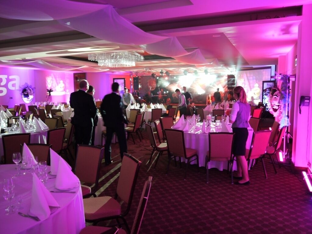 A banquet hall with round tables set for a formal event, featuring a chandelier and draped curtains.