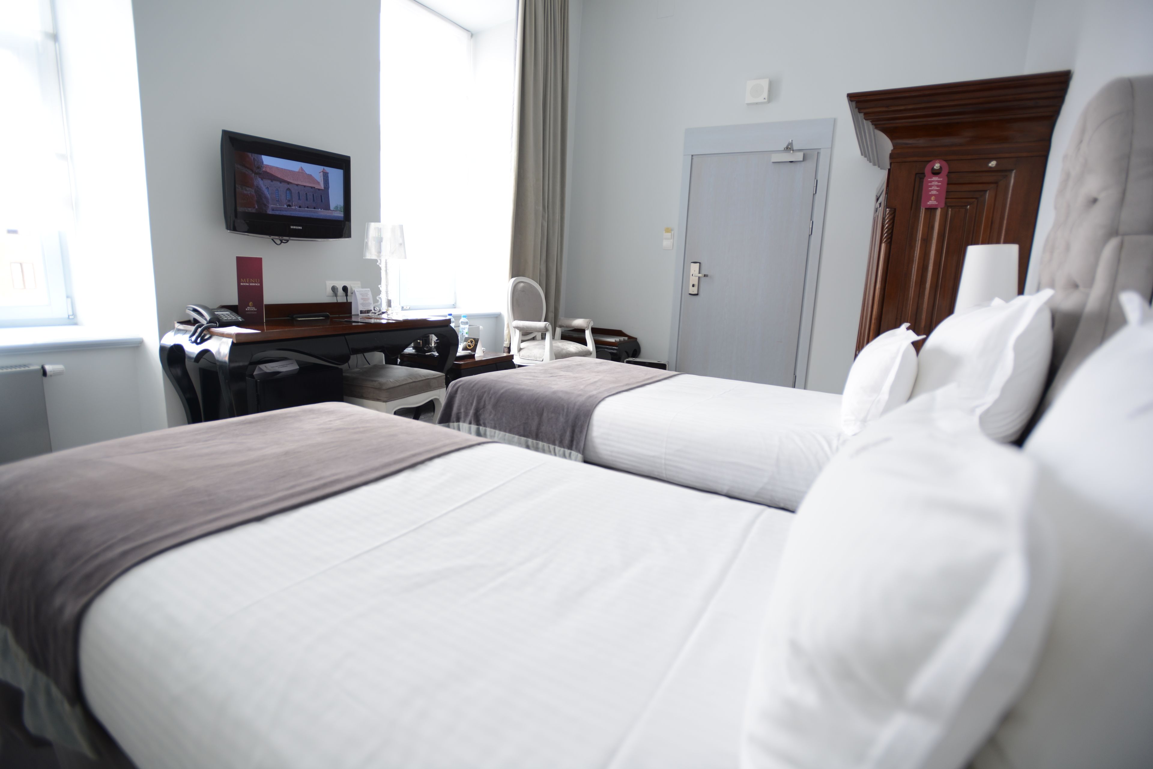 A hotel room with two beds, a desk with a computer, a TV mounted on the wall, and a door with a sign.