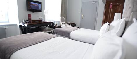 A hotel room with two beds, a desk with a computer, a TV mounted on the wall, and a door with a sign.