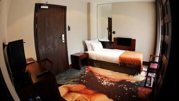 A hotel room with a bed, a desk, a chair, a TV, and a door.