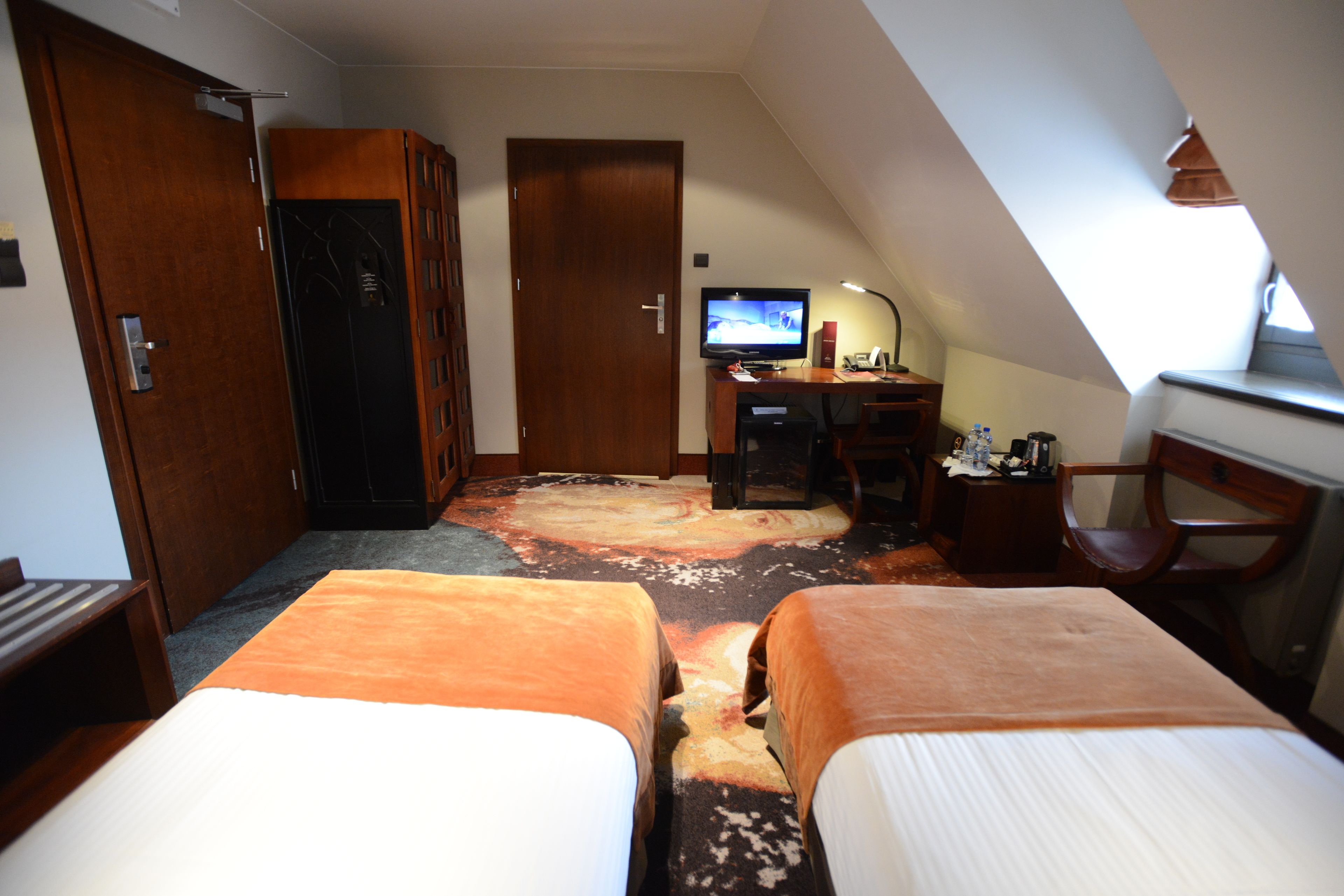 A hotel room with two beds, a desk with a television, and a large rug.