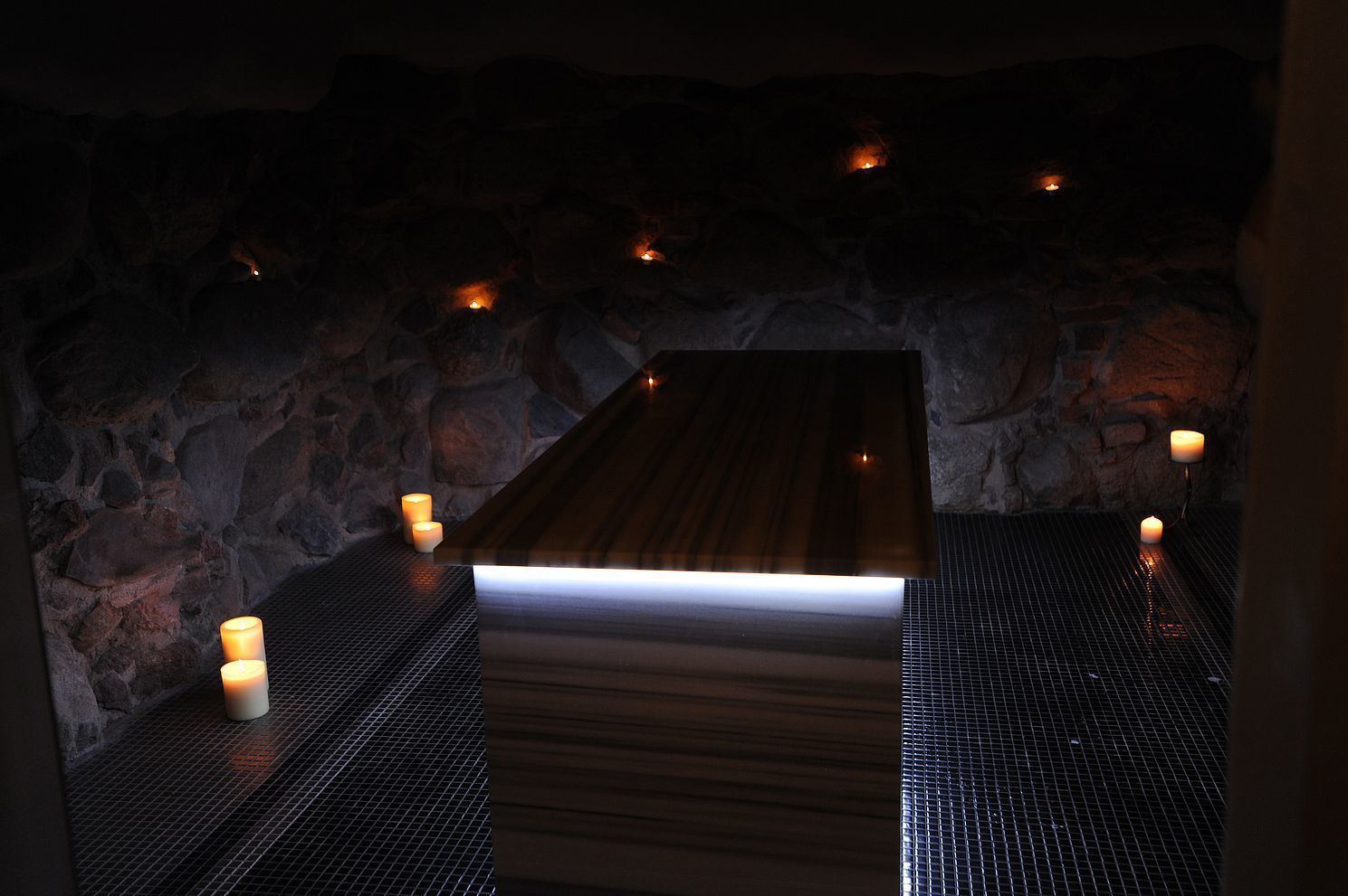 Un espacio de spa con banco de madera, paredes de piedra y velas.