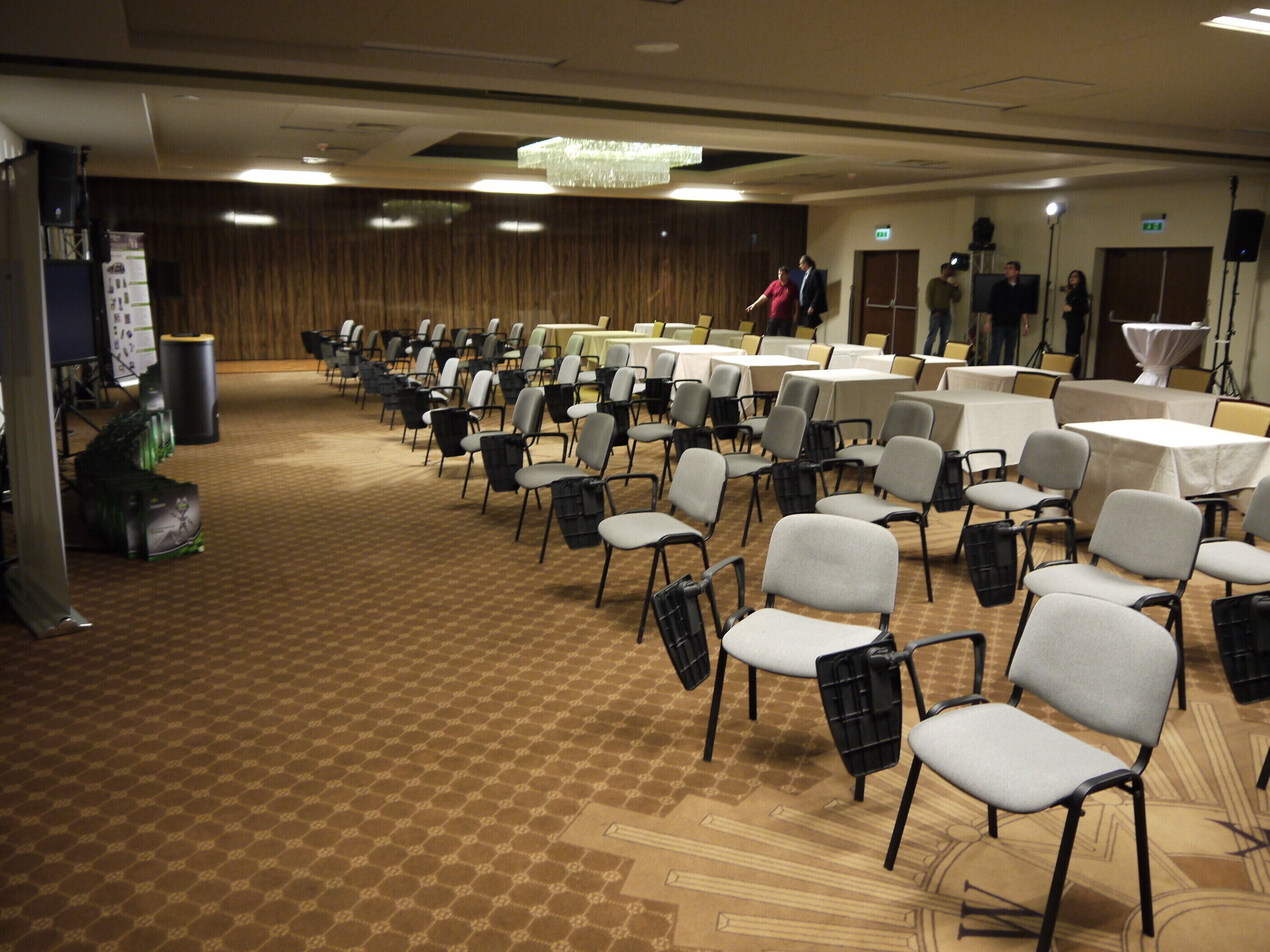 A conference room with rows of chairs and tables, a carpeted floor, and a chandelier.