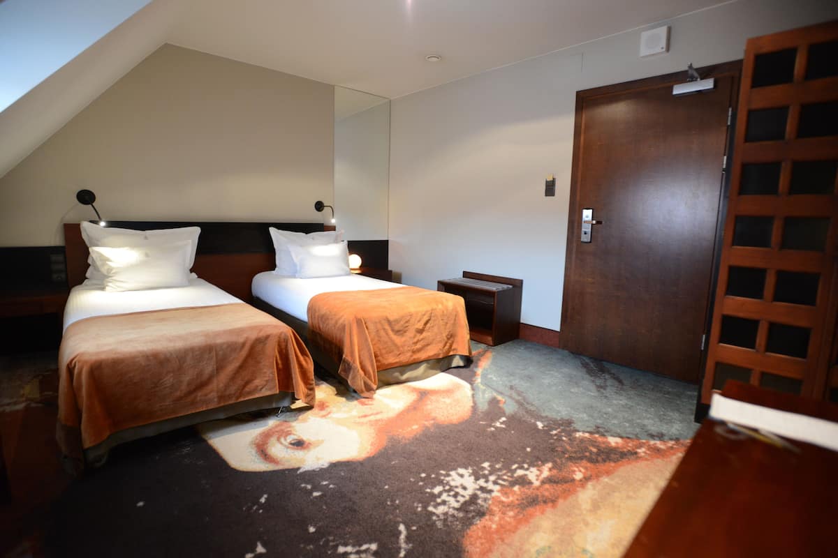 Ett hotellrum med två sängar, en stor spegel, en trädörr och en matta med ett fiskmönster.