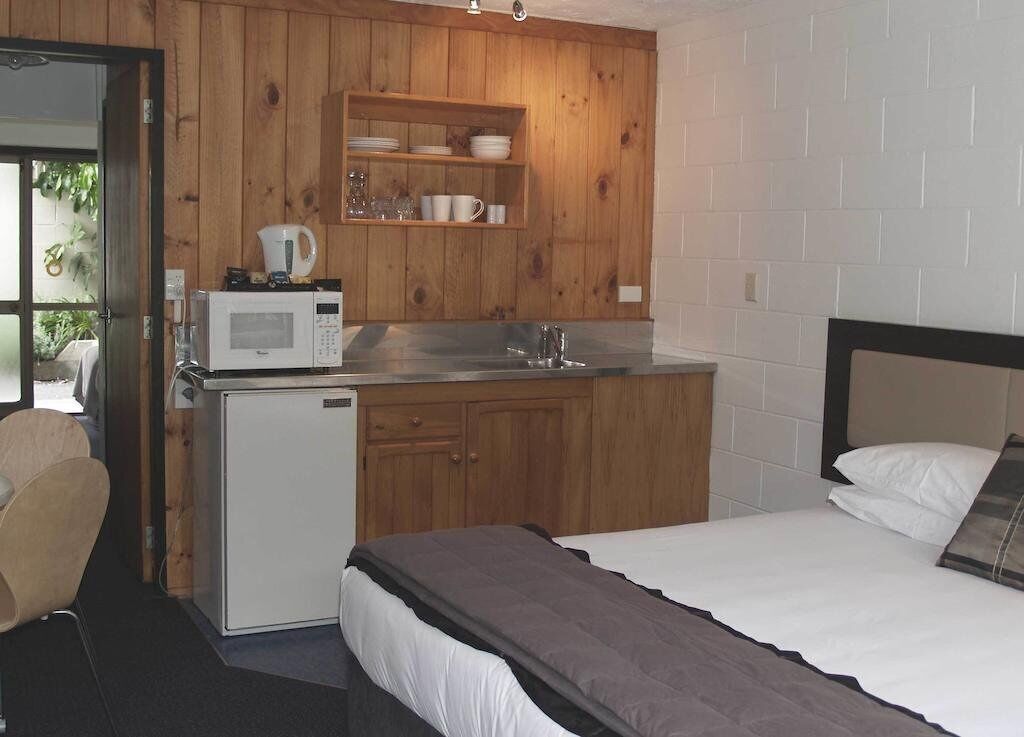 A compact room with a bed, a small kitchenette, and a door leading to a balcony.