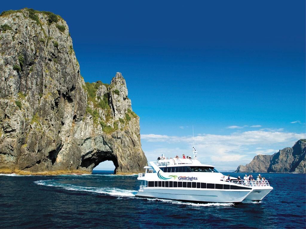Ein Boot mit der Aufschrift 'Great Sights', das nahe einer felsigen Küste mit einer markanten Felsbogenformation fährt.