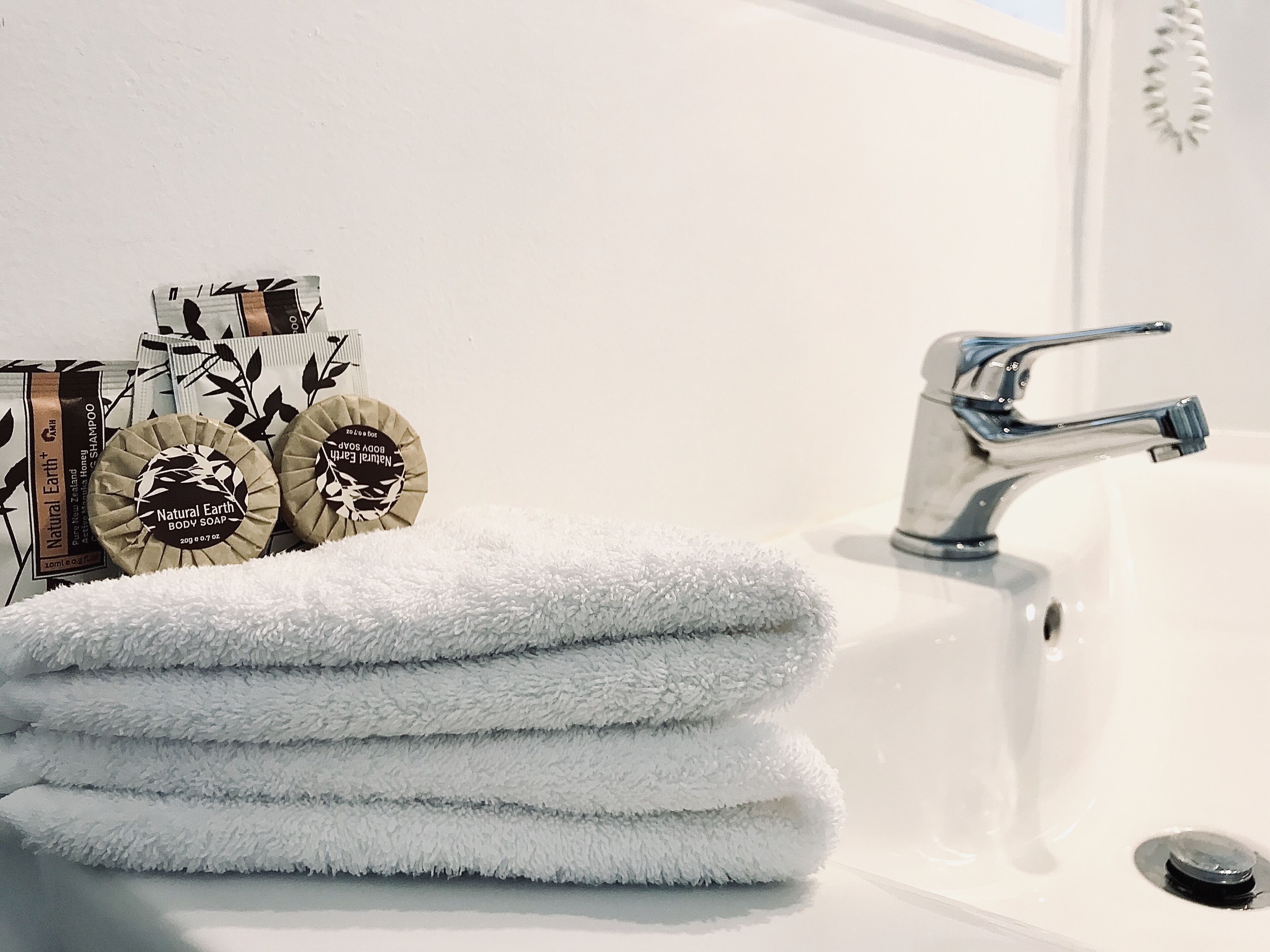 A bathroom with a white sink, a silver faucet, and a stack of white towels. There are two round soap bars with labels on the left side of the sink.
