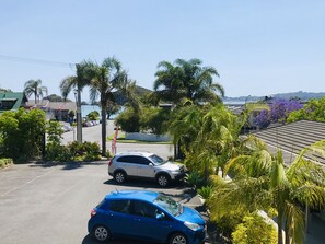Un estacionamiento con dos coches, palmeras y vistas a una masa de agua y colinas al fondo.