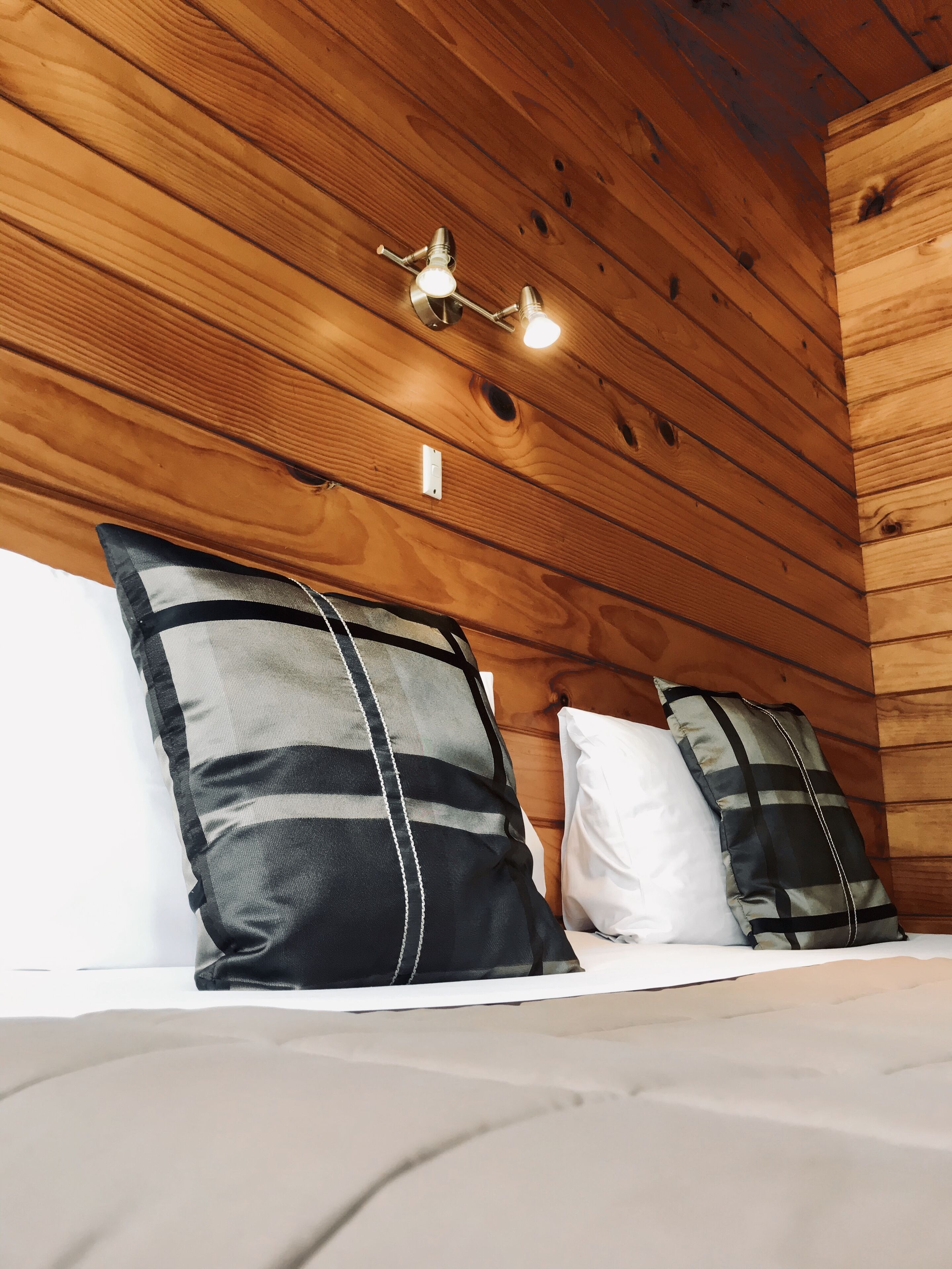 A wooden cabin interior with a bed, two pillows, and a wall-mounted light fixture.