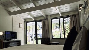 A hotel room with a bed, a television on a stand, a small table, and a window with curtains. - Bounty Motel (Paihia)