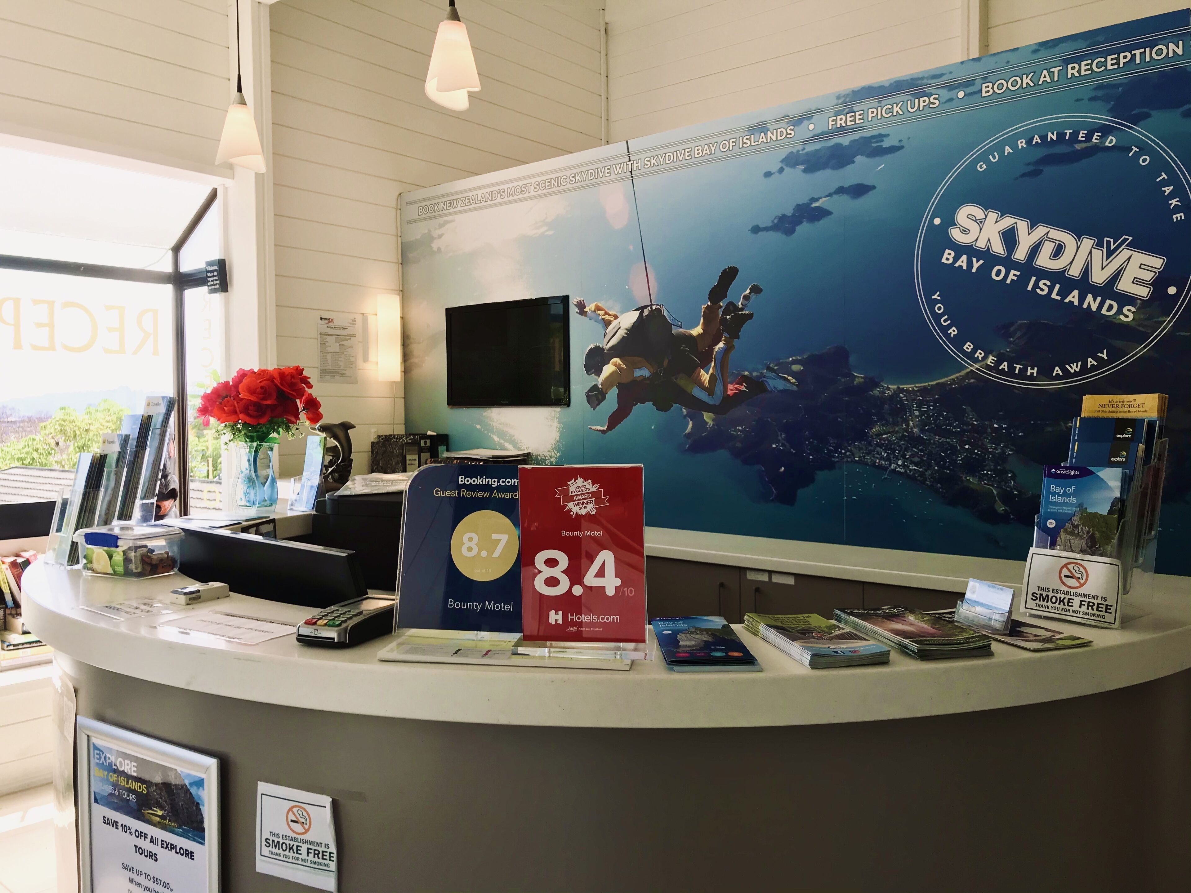 Una recepción con un cartel grande que anuncia SkyDive Bay of Islands, un premio por reseñas de huéspedes de 8.7, y un 10% de descuento en tours.