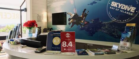 Una recepción con un cartel grande que anuncia SkyDive Bay of Islands, un premio por reseñas de huéspedes de 8.7, y un 10% de descuento en tours.