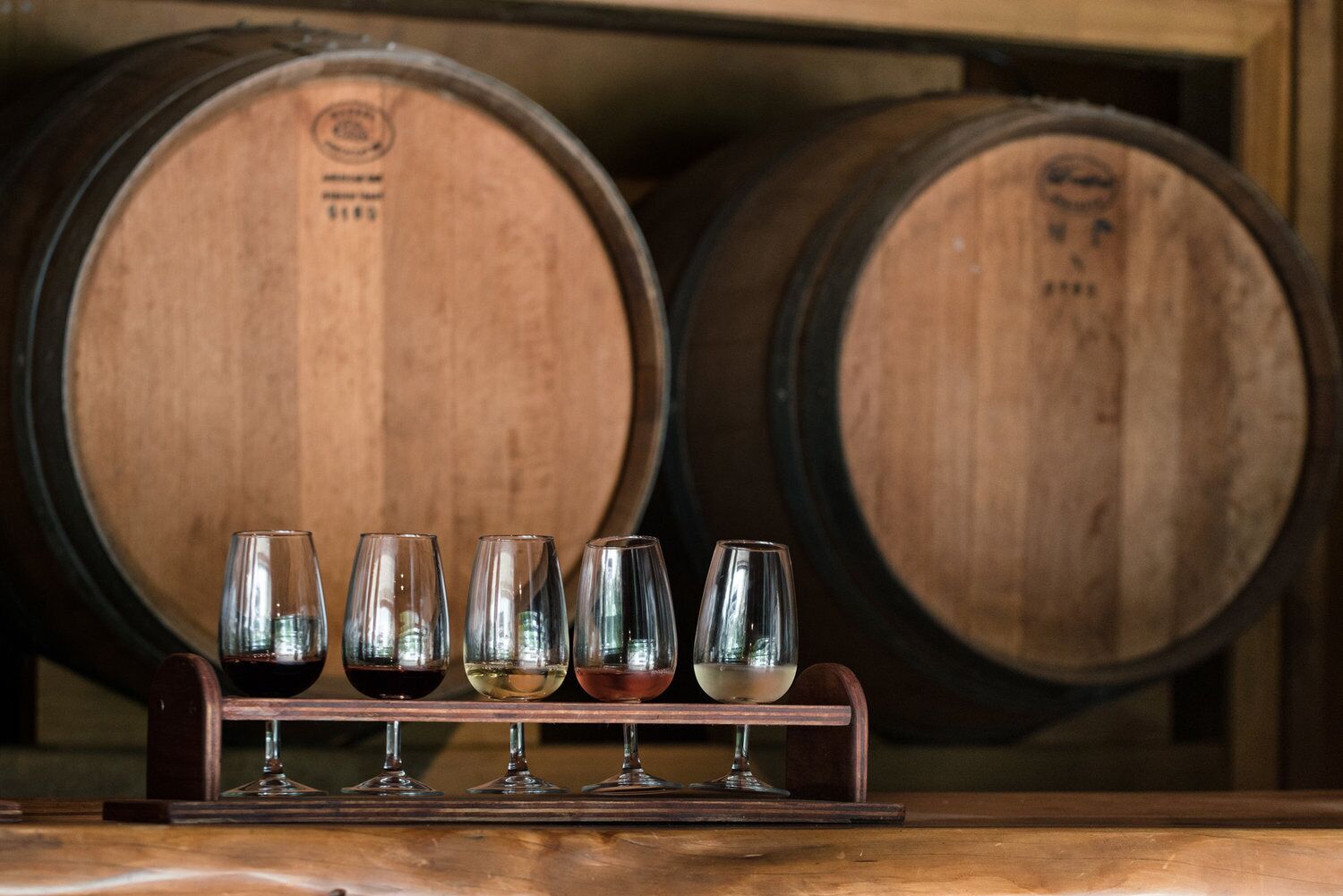 Wine glasses on a rack with wooden barrels in the background.