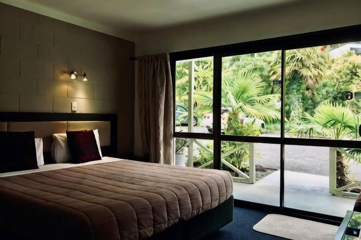 Ein Schlafzimmer mit einem großen Bett, einem Fenster mit Blick auf Grünflächen und einer Wandleuchte.