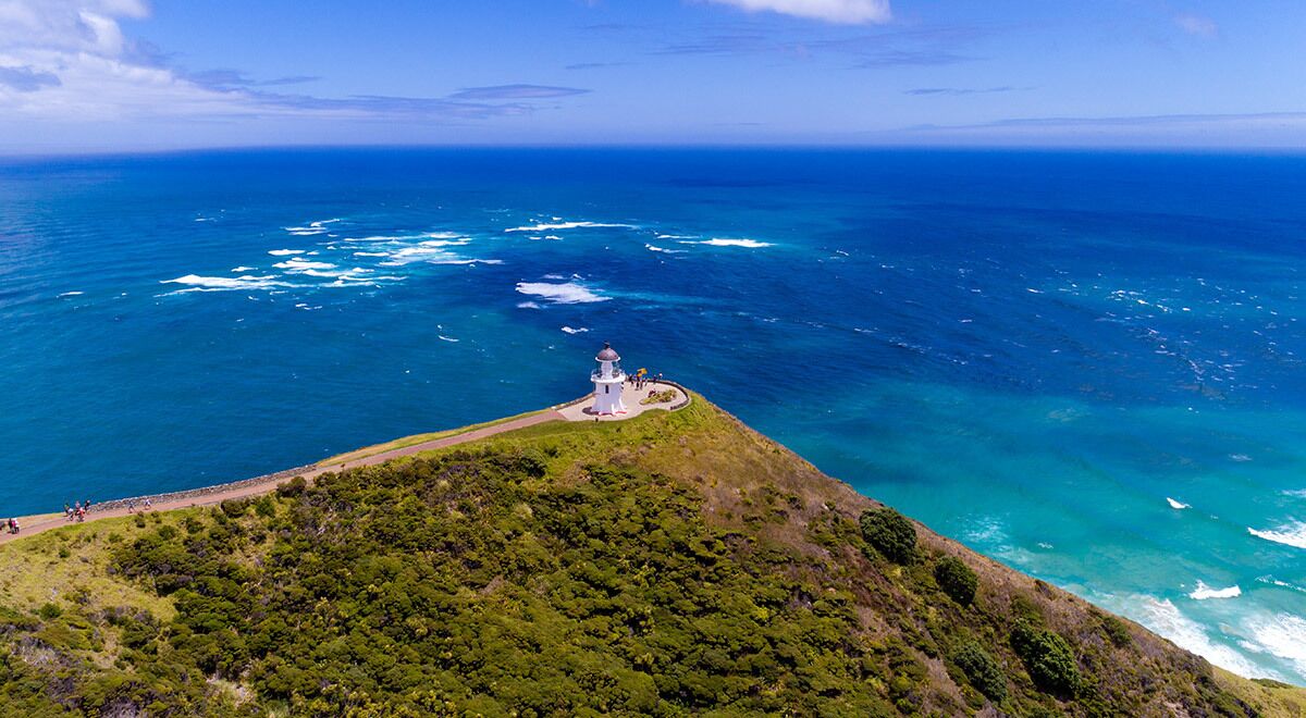 A lighthouse on a cliff overlooking a vast ocean with clear skies.