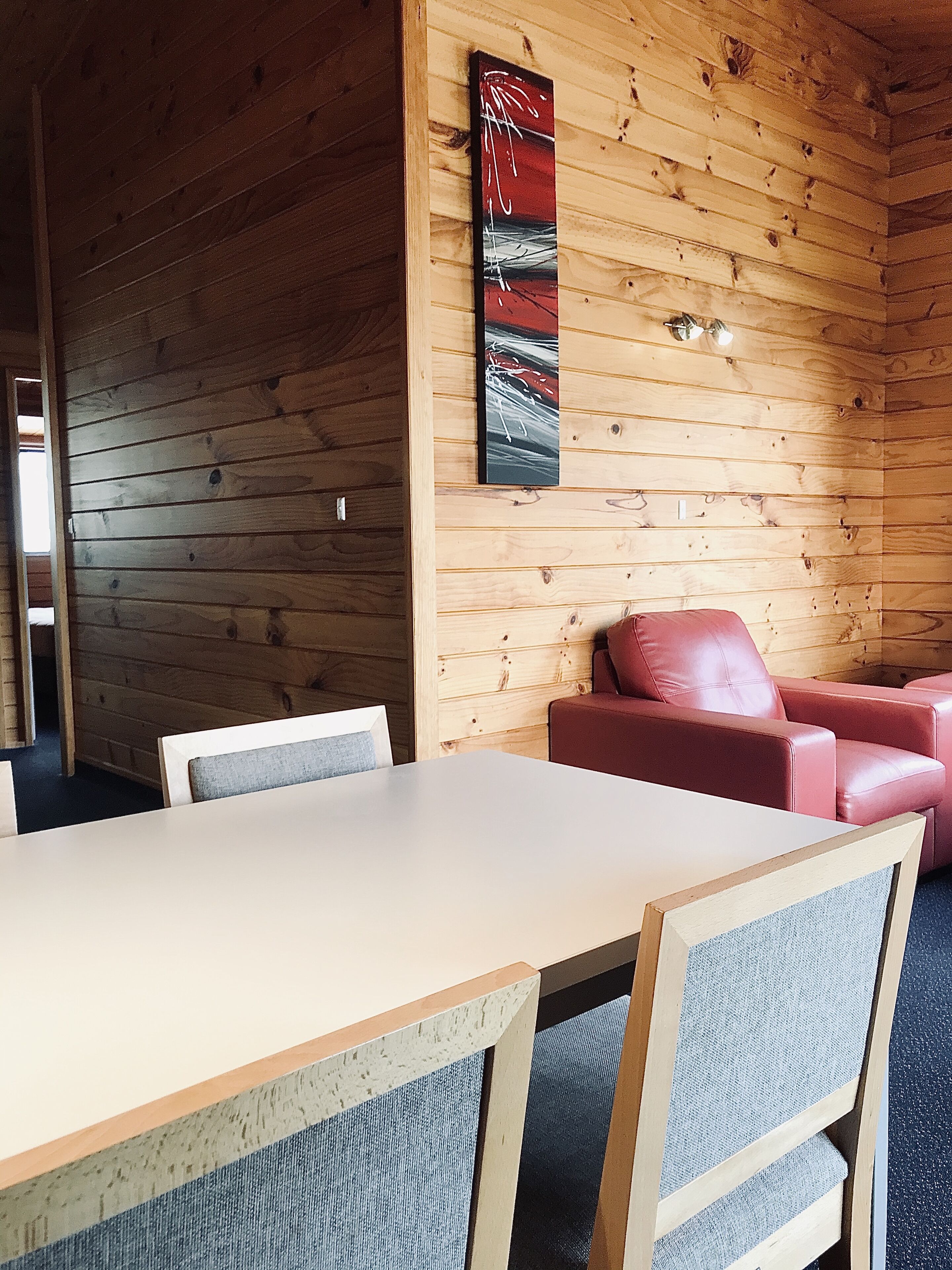 Un intérieur en bois comprenant une table à manger, des chaises, un canapé rouge et un tableau abstrait accroché au mur.