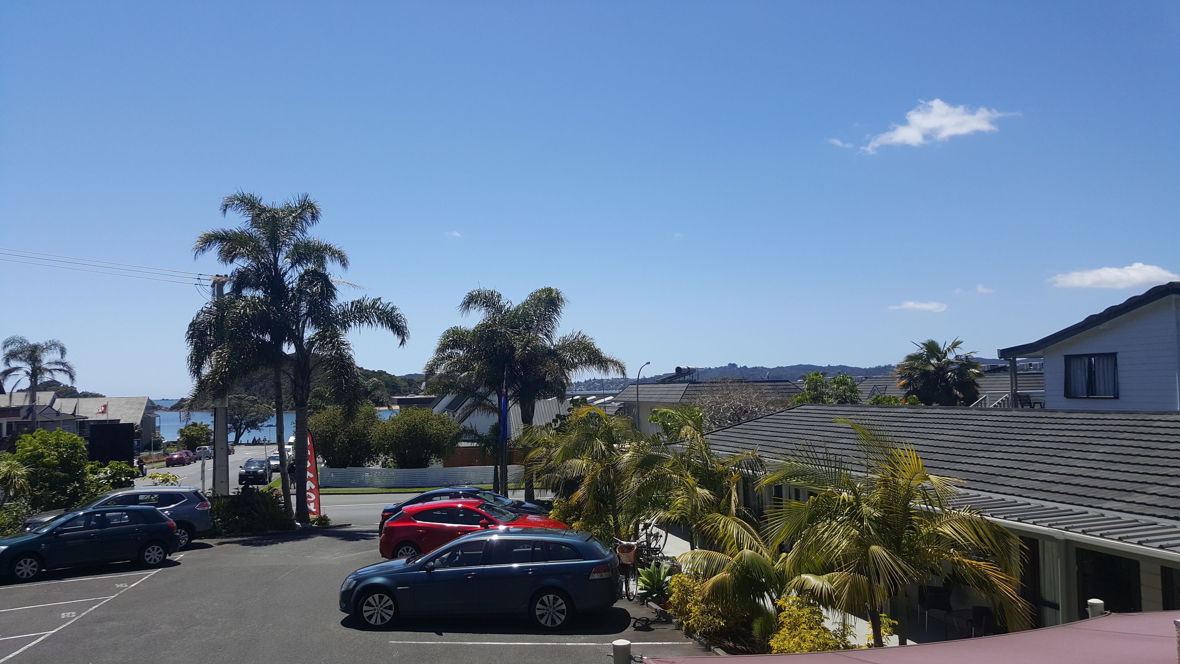 A parking lot with several cars, palm trees, and a building with a sloped roof.