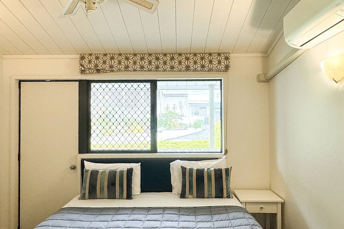 Ein Schlafzimmer mit einem Bett, einem Fenster mit Ausblick, einem Deckenventilator und einer Wand-Klimaanlage.