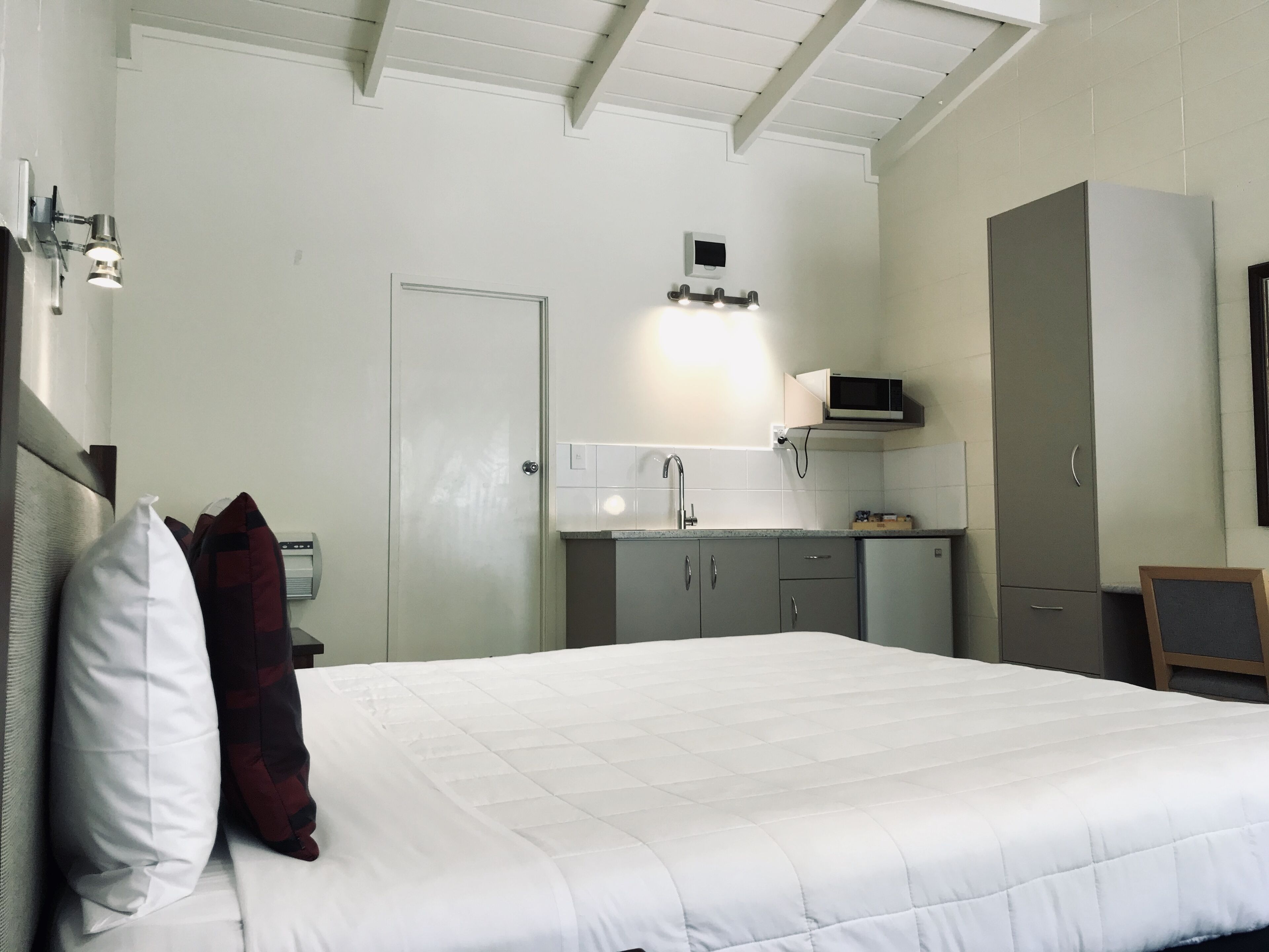 Une chambre avec un lit, une armoire, un petit coin cuisine et une porte.
