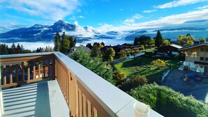 A balcony with a view of a mountain range, a forested area, and a small village. - Le Floralp (Combloux)