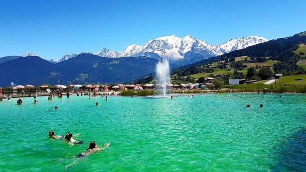 A large outdoor swimming pool surrounded by mountains, with people swimming and sunbathing. - Le Floralp (Combloux)