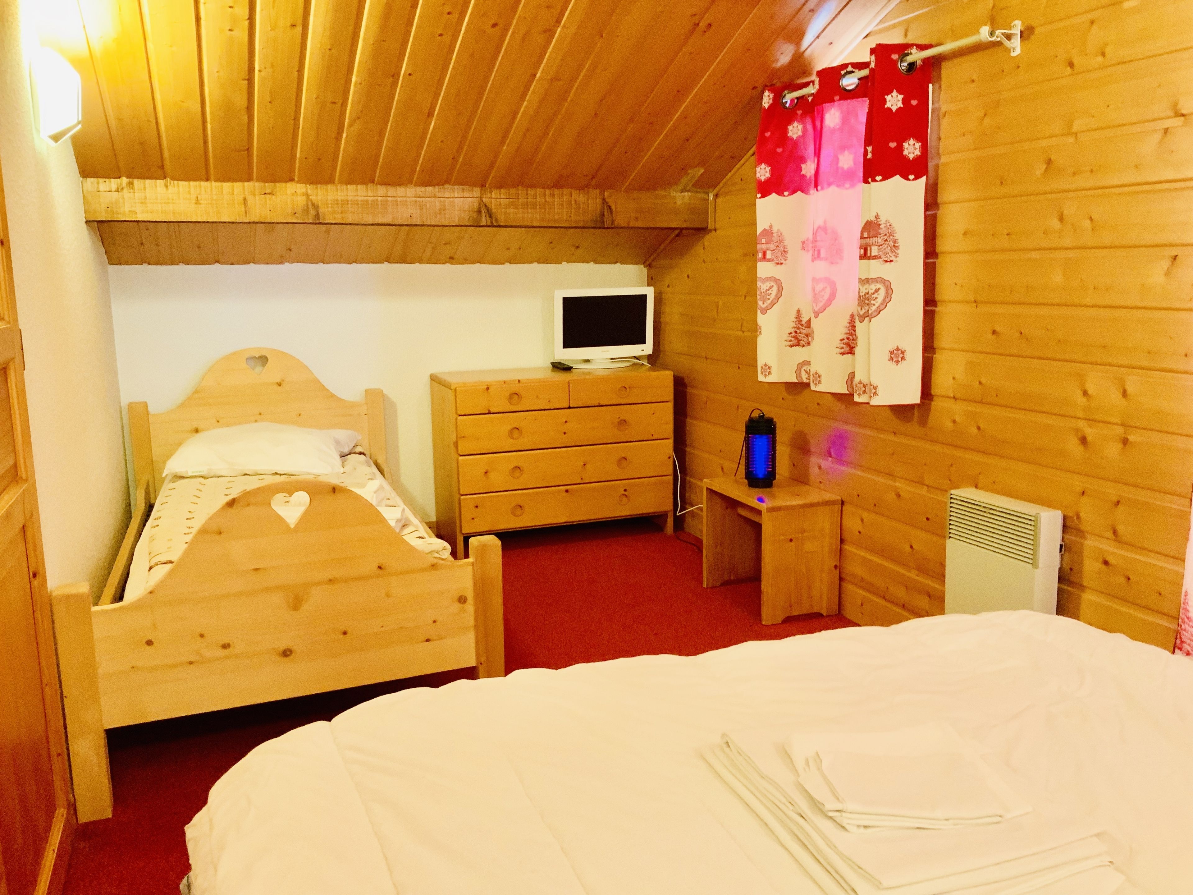 A wooden room with a bed, a dresser, a TV, a heater, and a curtain.