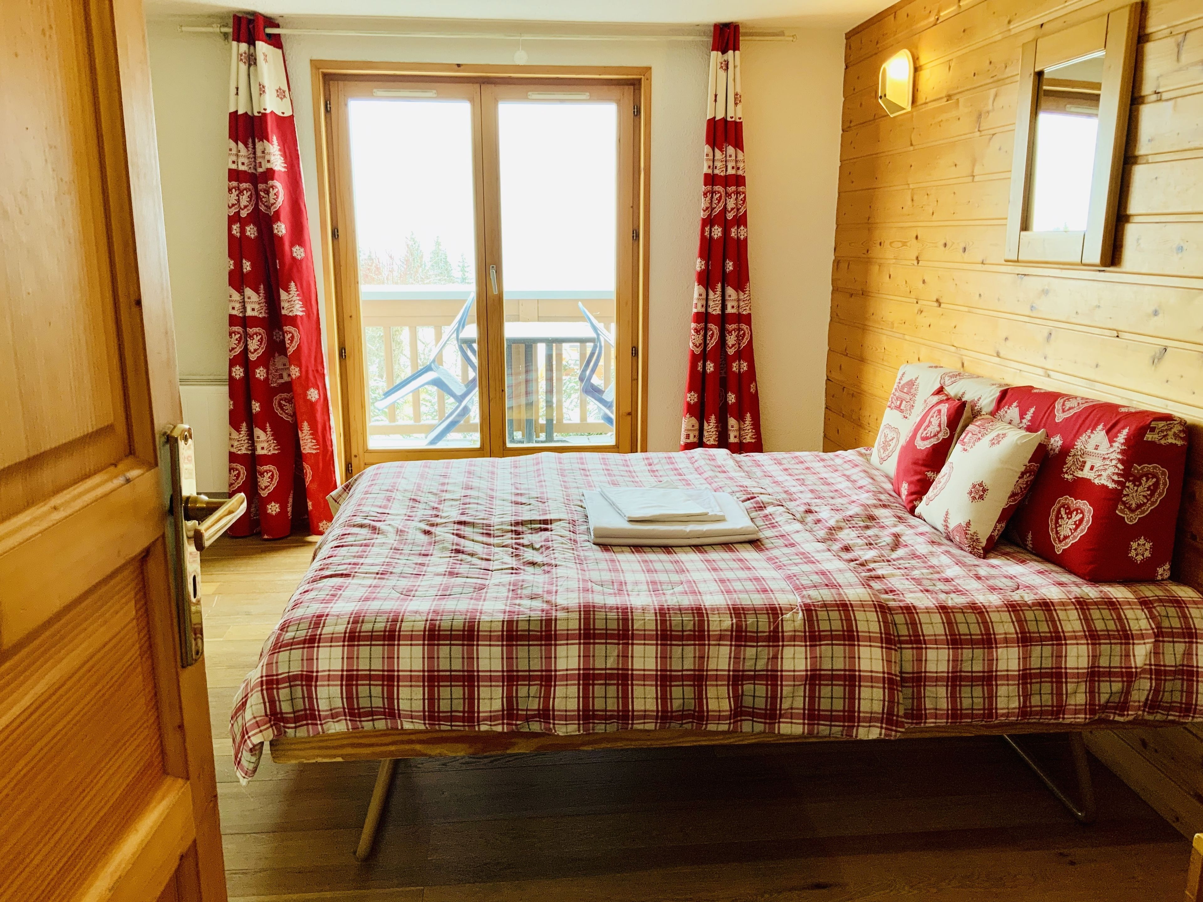 Una camera da letto con un letto, tende, una testiera in legno e una finestra con vista su un balcone.