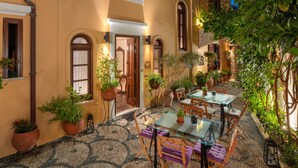 An outdoor patio with a glass table and chairs, surrounded by potted plants and a cobblestone floor.