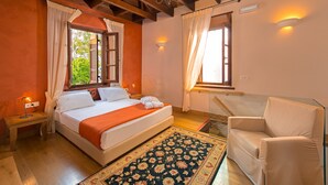 A bedroom with a bed, a chair, a nightstand, a chandelier, and a window with curtains.