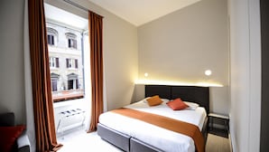 A hotel room with a large bed, a bench by the window, and a view of a building outside. - The Roman Empire Guesthouse (Rome)