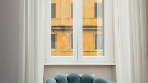 A room with a blue armchair, a yellow pillow, and a window with white curtains. - The Roman Empire Guesthouse (Rome)