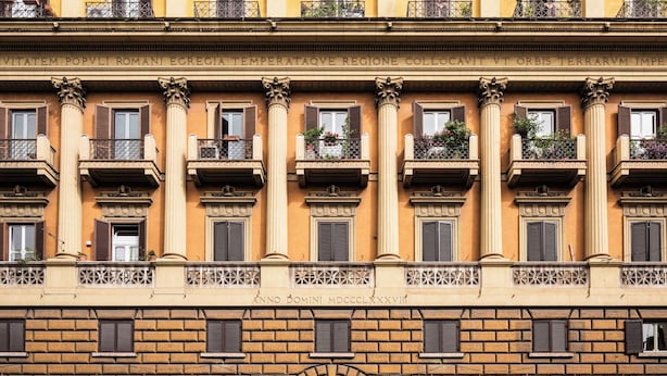 A multi-story building with a yellow facade, large windows with shutters, and balconies with plants. - The Roman Empire Guesthouse (Rome)