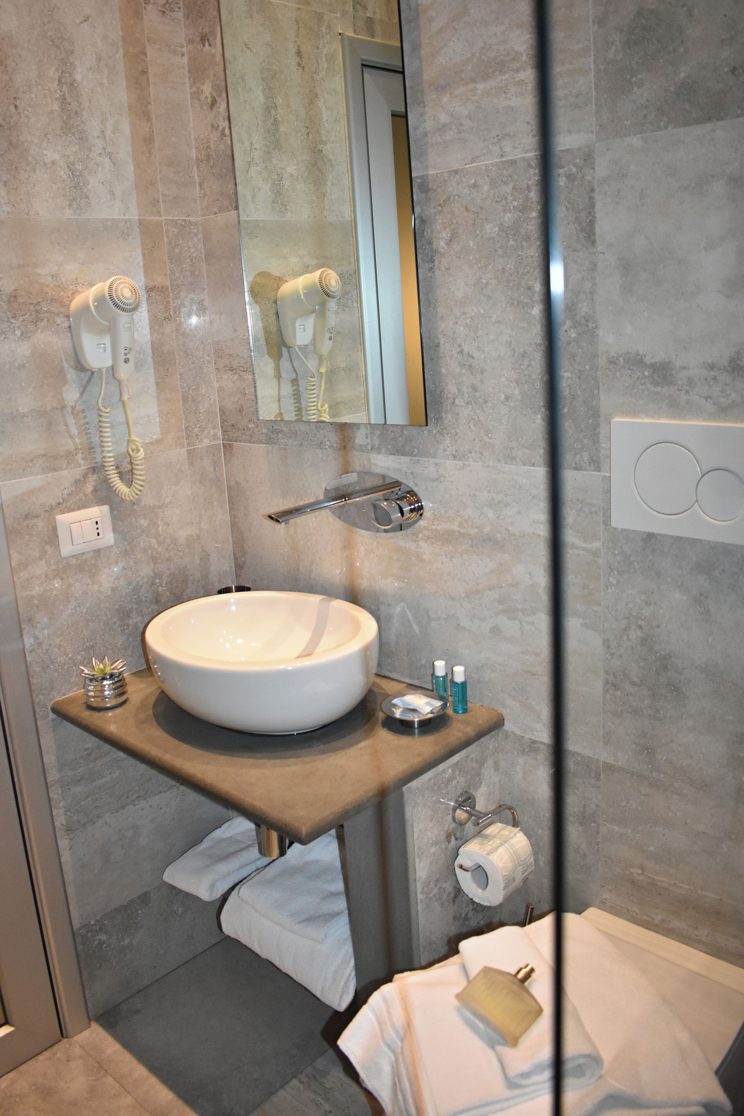 Un baño moderno con un lavamanos grande, un secador de pelo, un perchero para toallas y un dispensador de papel higiénico.