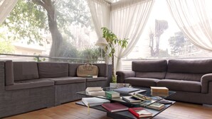 A living room with two grey sofas, a glass coffee table with books, a lamp, and a plant. - Villa Pirandello (Rome)