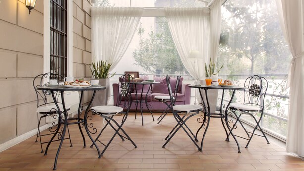 A covered patio with a table and chairs, a sofa, and potted plants. - Villa Pirandello (Rome)