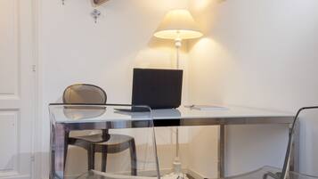 A modern office space with a desk, two chairs, a laptop, a lamp, a bookshelf, and a painting on the wall.