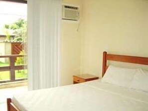A single-bed room with a wooden headboard, a small bedside table, and a window with a view of greenery outside. - Pousada Praia Bella (Búzios)