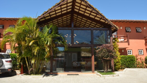 A building with a modern glass facade, a wooden roof, and a palm tree in the foreground. - Pousada Praia Bella (Búzios)