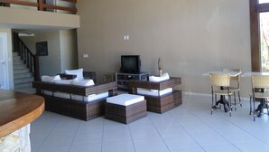 A spacious living area with a high ceiling, a television, wicker furniture, and a dining area with wicker chairs. - Pousada Praia Bella (Búzios)