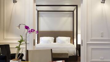A hotel room with a bed, a desk with a laptop, a chair, a potted orchid, and two wall-mounted lamps.