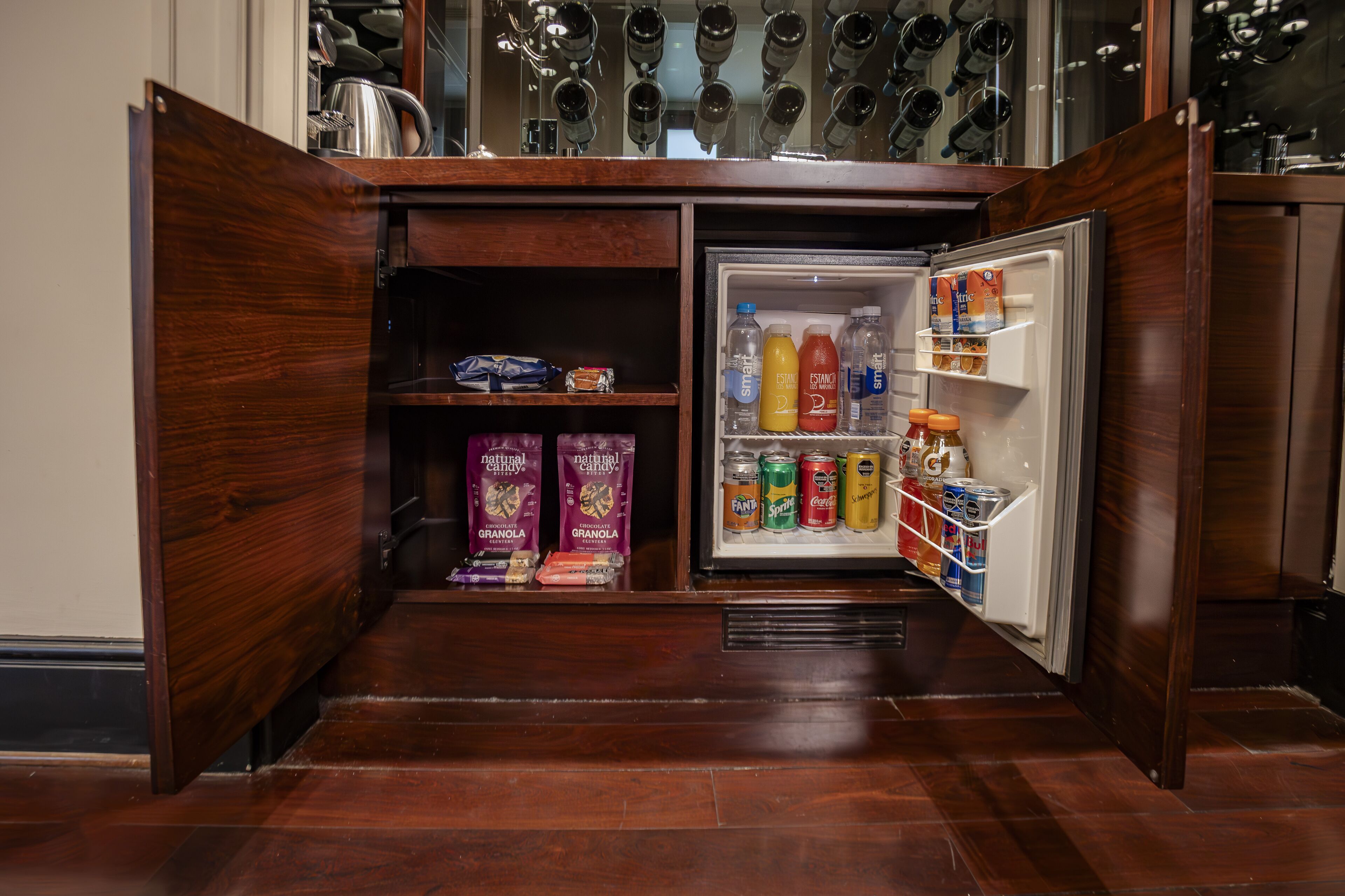 A compact kitchen with a built-in refrigerator stocked with beverages and snacks.
