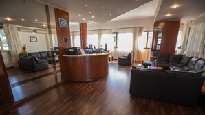 A hotel lobby with a reception desk, seating area, and large windows. - Hotel Rossi (Domagnano)