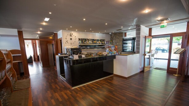 A bar area with a wooden floor, a counter with a glass display, and a wall with a clock. - Hotel Rossi (Domagnano)