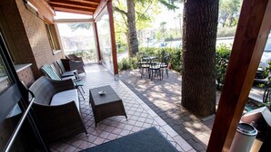 A covered outdoor seating area with wicker furniture and a table, a tree, and a view of the street. - Hotel Rossi (Domagnano)