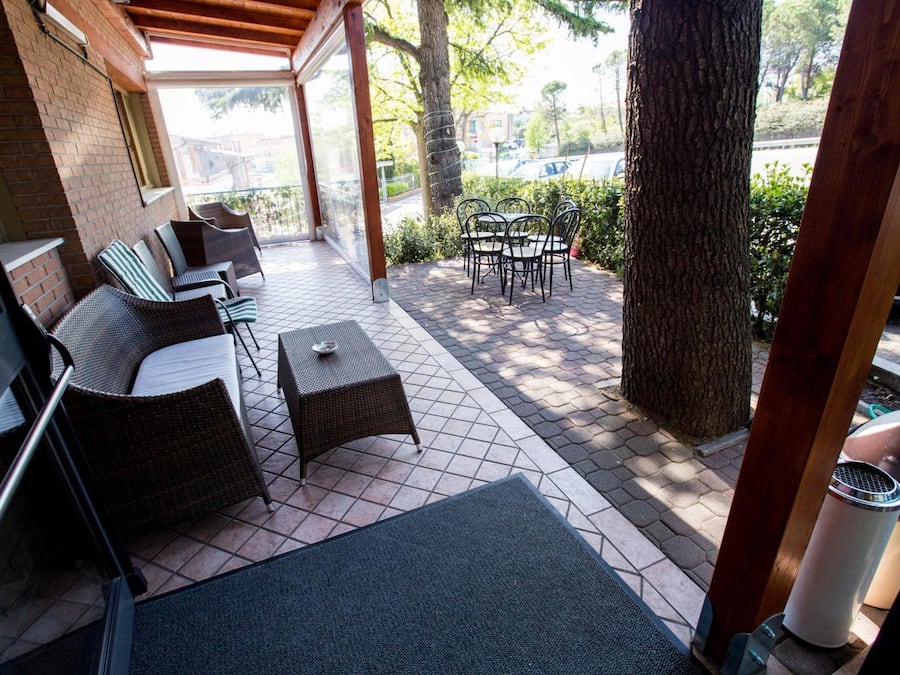 A covered outdoor seating area with wicker furniture and a table, a tree, and a view of the street.