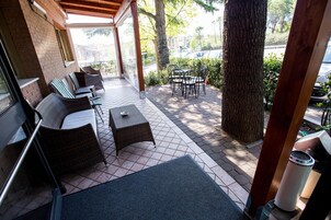 Un espacio de estar al aire libre cubierto con mobiliario de mimbre, una mesa, un árbol y vistas a la calle.